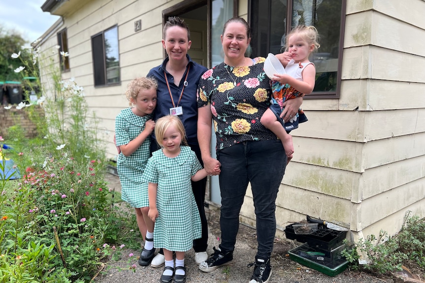 a family of a woman, a person and three young girls holding hands and looking at the camera