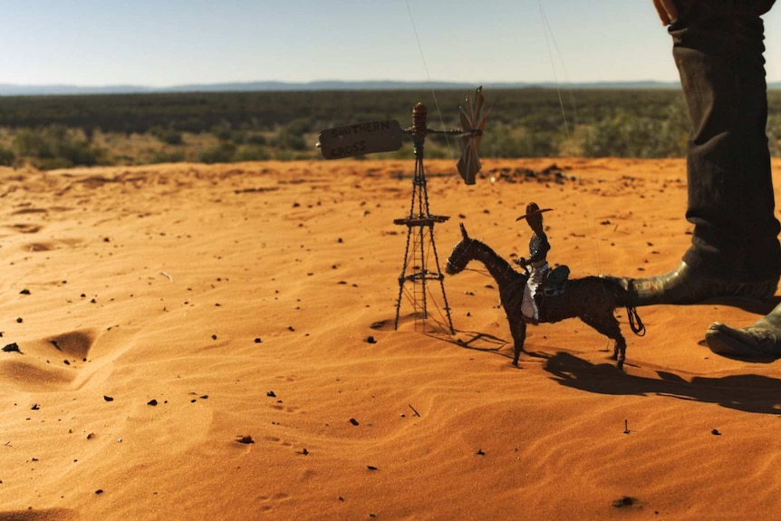 A tiny puppet of a man on a horse, standing near a tiny windmill with a sign on it reading: Southern Cross, in the outback.