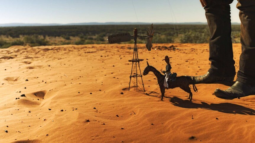 A tiny puppet of a man on a horse, standing near a tiny windmill with a sign on it reading: Southern Cross, in the outback.