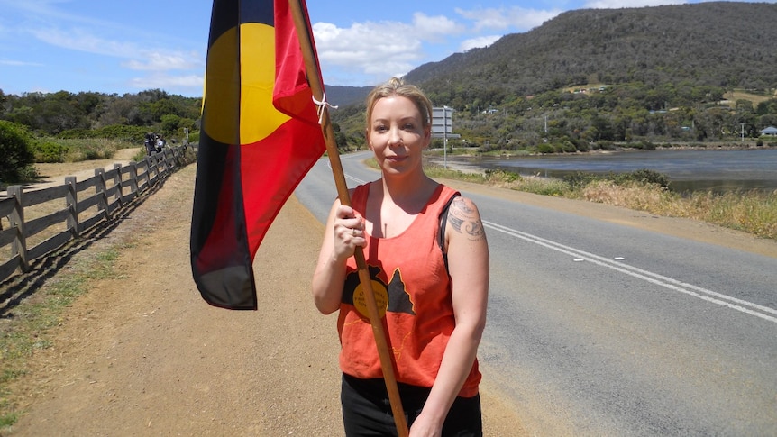 A young woman stands on the road holding an Aboriginal flag