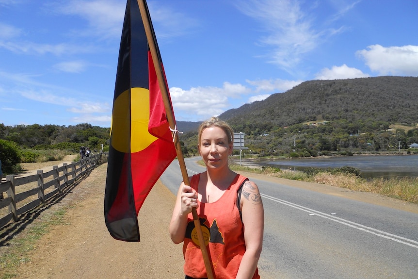 A young woman stands on the road holding an Aboriginal flag