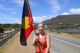 A young woman stands on the road holding an Aboriginal flag