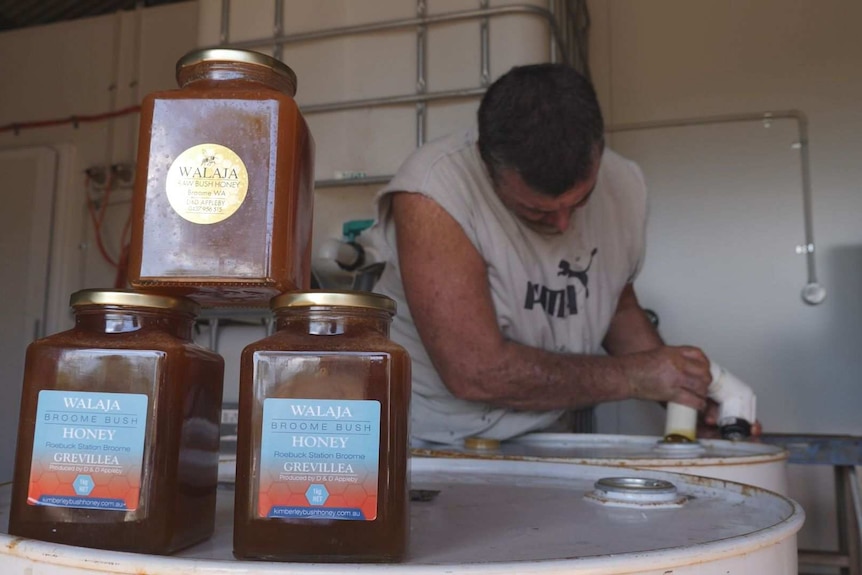 Man leaning over behind jars of honey