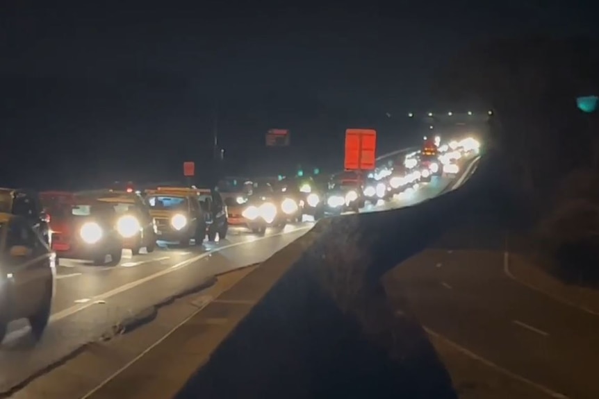 Traffic stretching back along a main road in the dark, with headlights of cars flashing