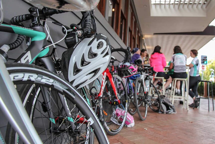 Close up of bikes propped against a wall in the foreground with women at a bar in the background