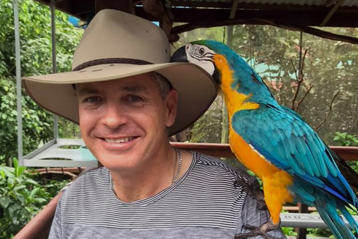 Anthony Di Salvo stand on a balcony with a Macaw parrot on his shoulder.