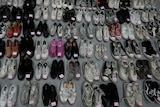 About 50 crumbled shoes in neat rows including converse, vans and a pair of pink slippers