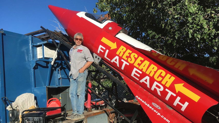 Mike Hughes stands in front of a large red rocket with Research Flat Earth written on the side