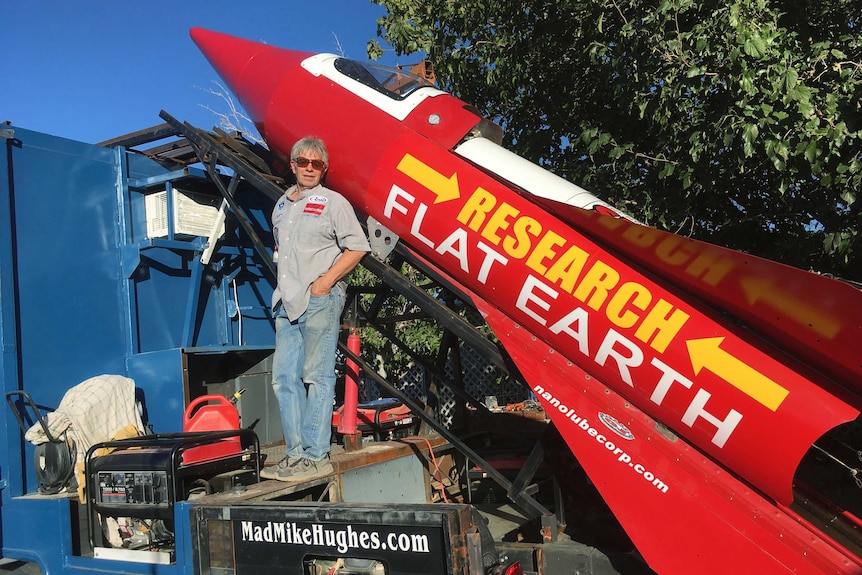 Mike Hughes stands in front of a large red rocket with Research Flat Earth written on the side