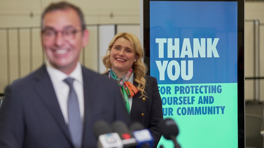 A sign saying thank you for being vaccinated stands behind a man and woman smiling