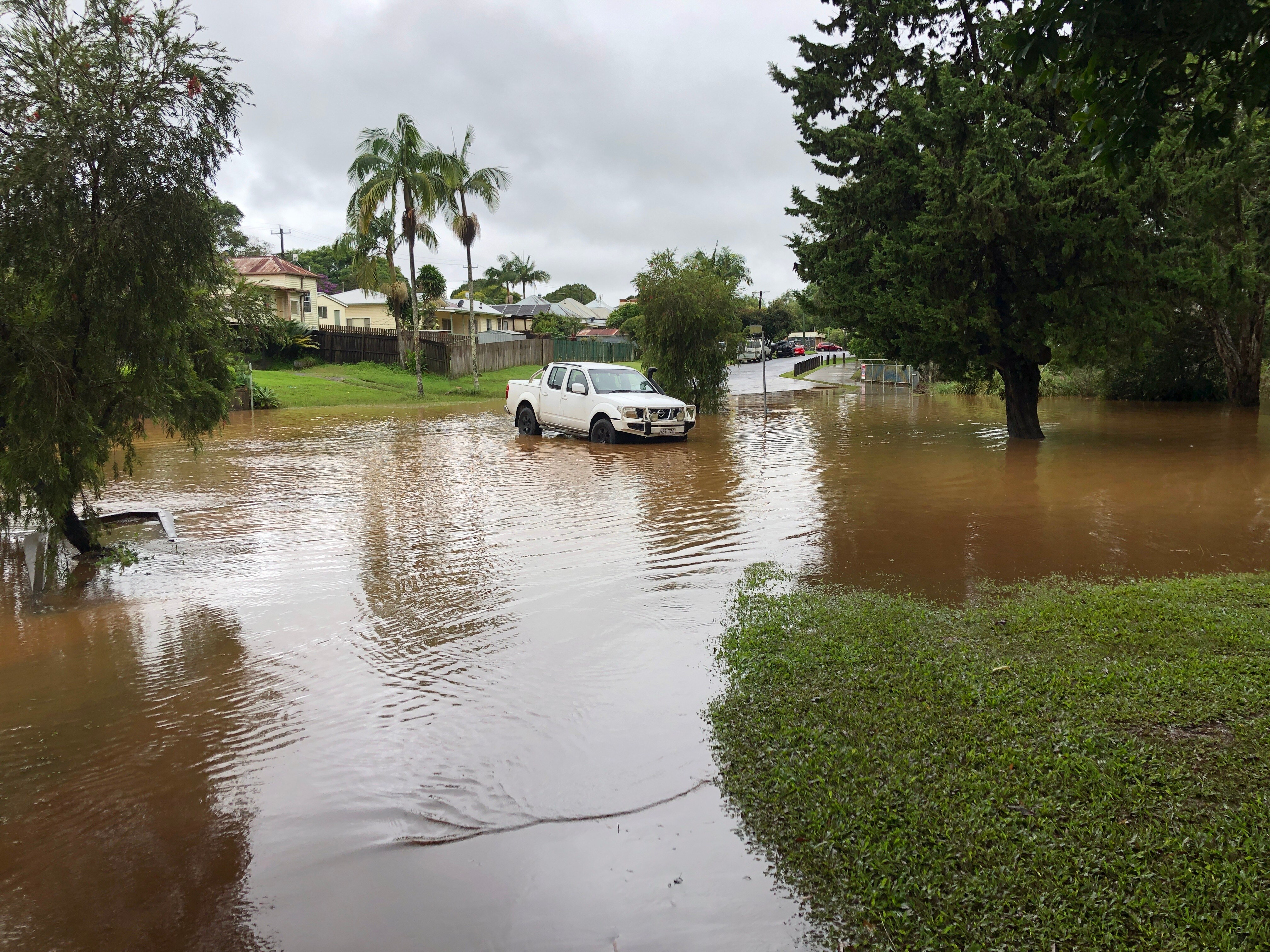 White car at the edge of a large body of water with houses behind it.
