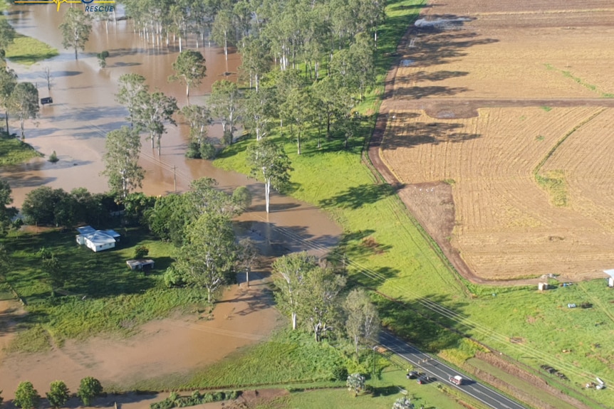 An aerial shot of flooded country, with a house close to be cut off by the rising flood water.