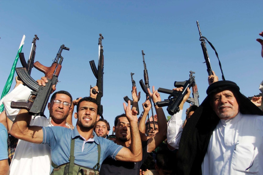 Iraqi tribal fighters shout slogans while holding weapons in Basra.