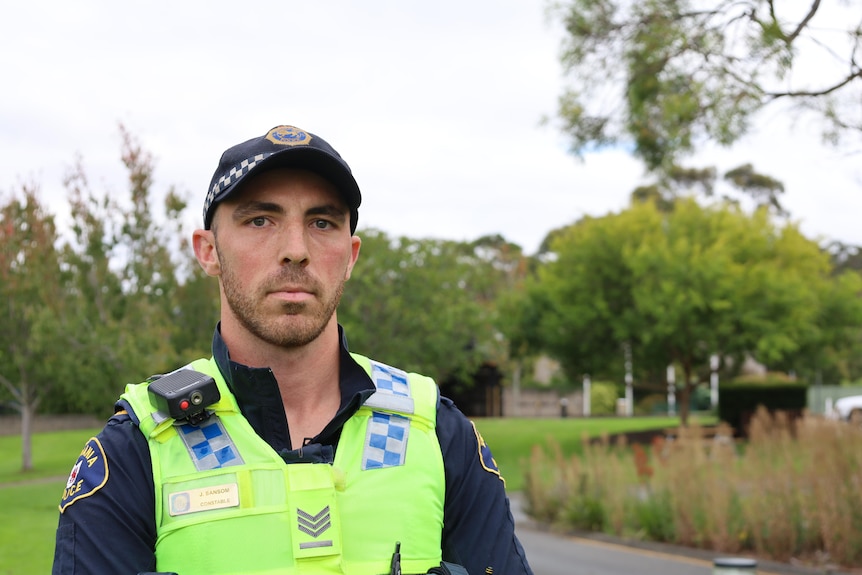 A man in a police uniform stands in front of trees