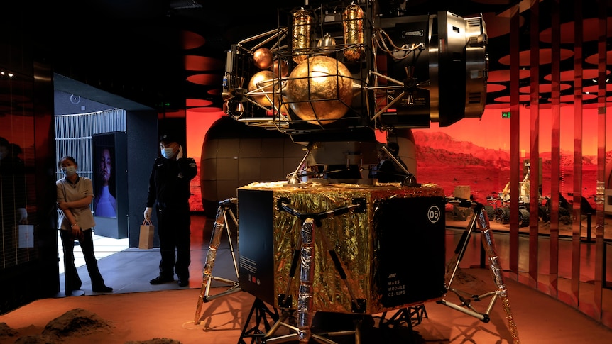 A security guard and worker stand near a depiction of a Chinese lander.