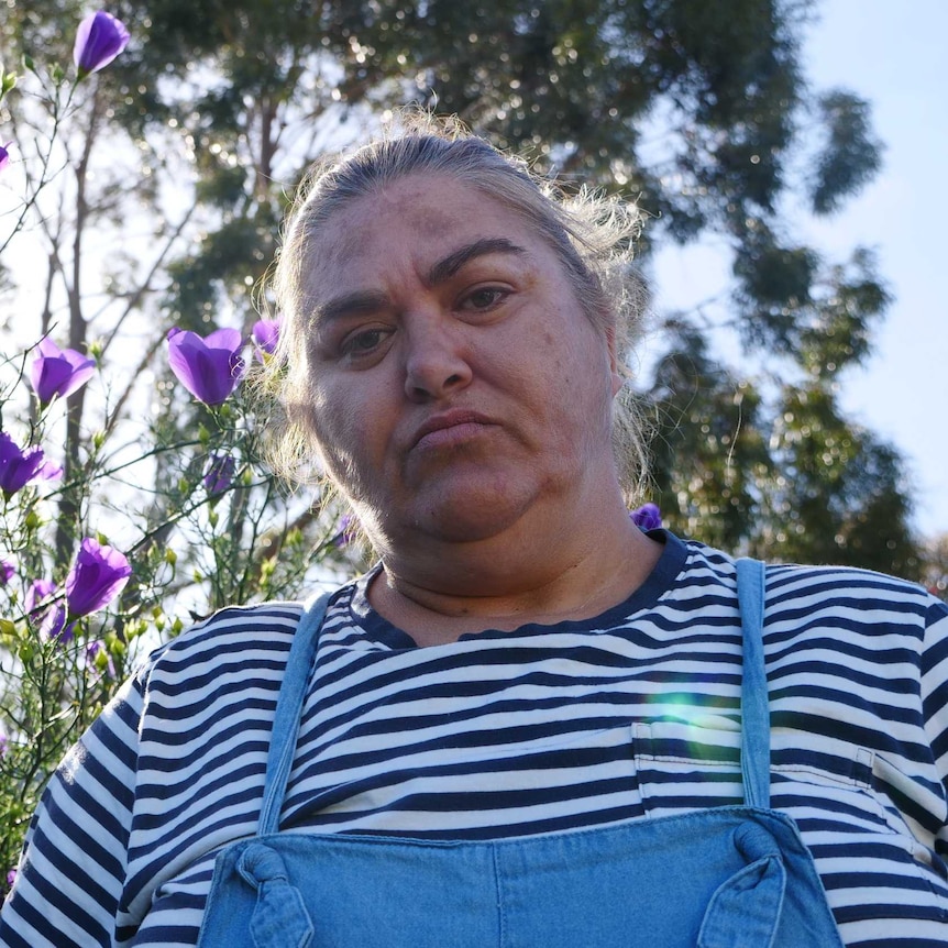 Woman Veronica Heritage-Gorrie stand in front of purple flower bush in backyard