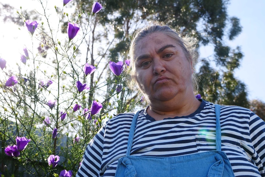 Woman Veronica Heritage-Gorrie stand in front of purple flower bush in backyard