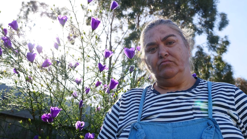 Woman Veronica Heritage-Gorrie stand in front of purple flower bush in backyard