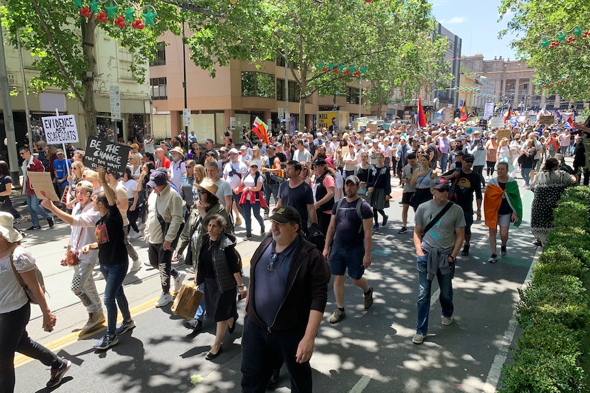 Crowd on people on a Melbourne street carry signs.