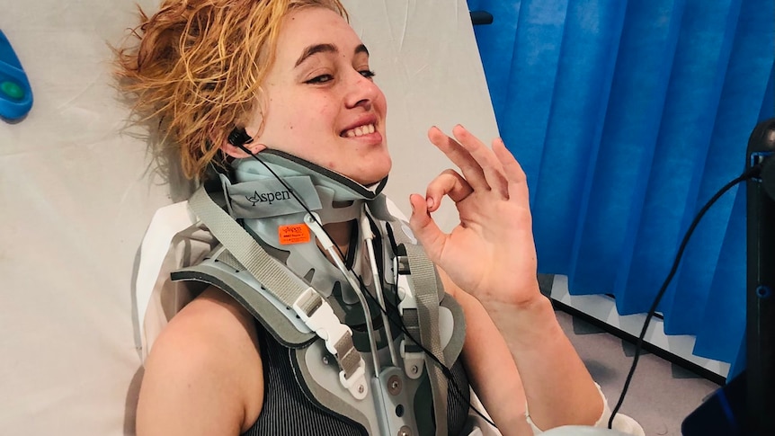 A teenager sits in a hospital bed with a neck brace on. 