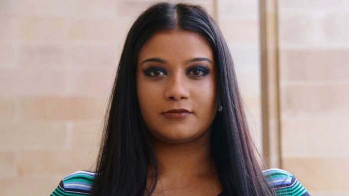 Woman with long dark hair and green-and-blue-striped top looking directly at the camera.