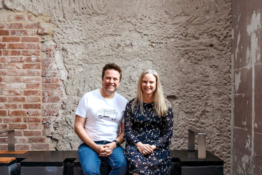A couple sit in front of an old rendered wall.