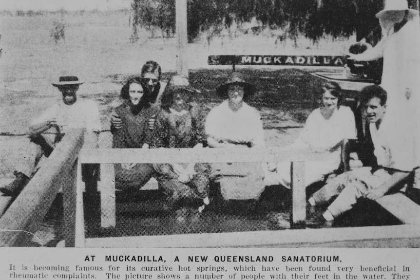 A black and white photo of a group of people sitting with their feet in an artesian bath in Muckadilla