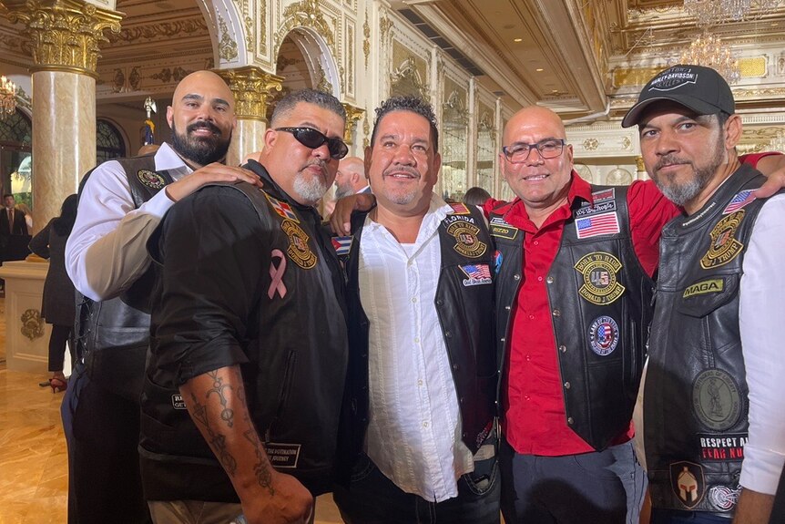 A group of men in leather vests in an opulent ballroom