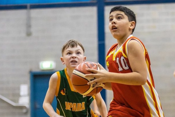 Junior basketballer in a red top with a ball running down a basketball court