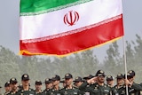 Rows of Iranian servicemen stand on guard under a large Iranian flag.