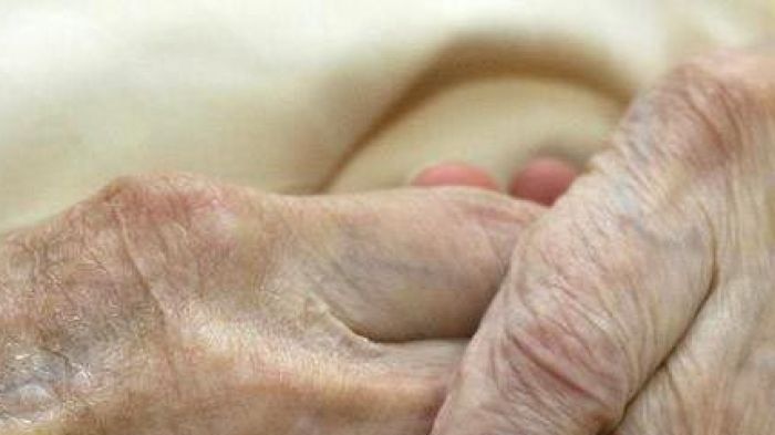 A young carer holds the hands of an elderly woman in a nursing home.