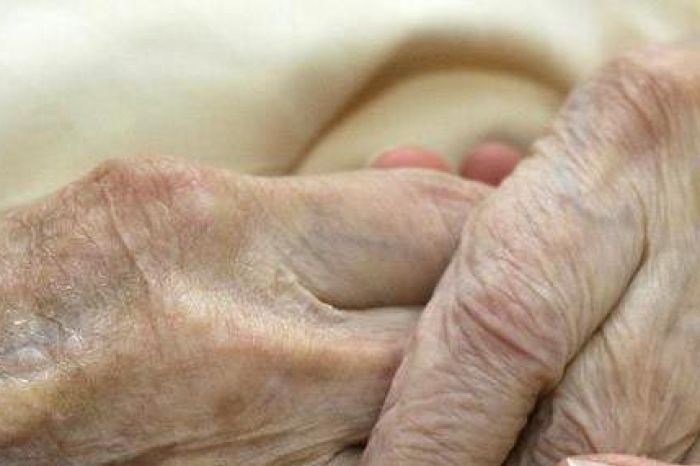 A young carer holds the hands of an elderly woman