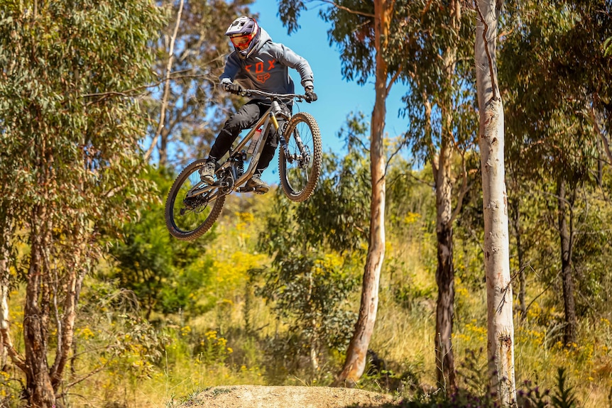 Man on a mountain bike over a trail jump. 