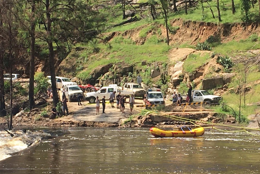 A bright yellow boat is pulled across a flooded river with ropes as crowds watch on the other side