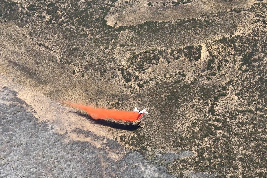 Aircraft over fire ground dropping orange retardant
