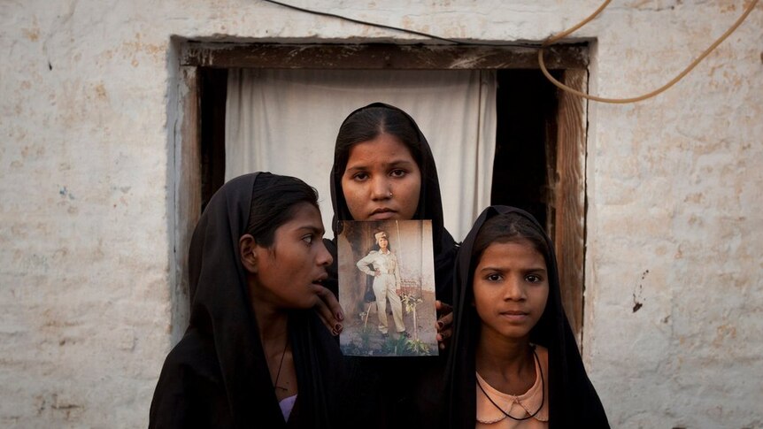 Three girls wearing headscarves look sad whilst holding up a photo of their mother, Asia Bibi.