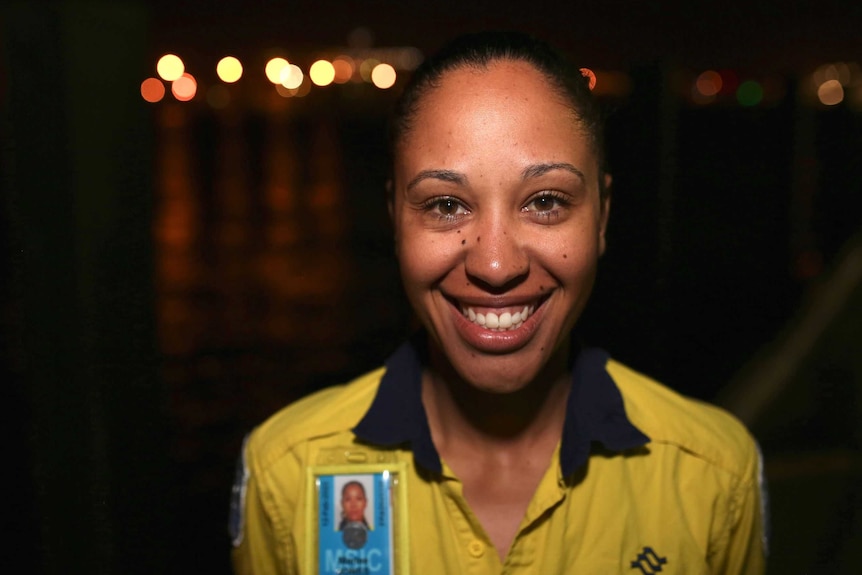 A woman in a yellow top with a name badge standing at a port at night.