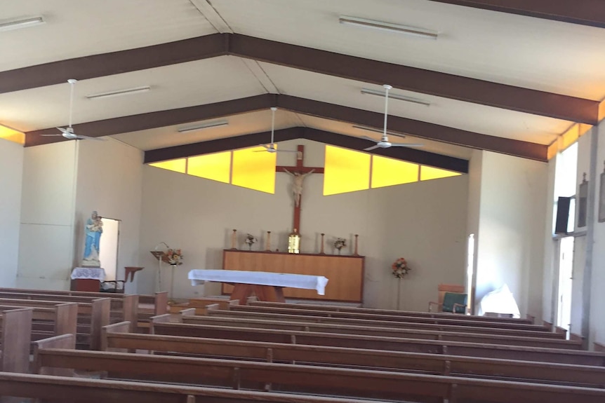 Inside a plain 1950s building with church pews, a statue of Mary and Catholic church altar.