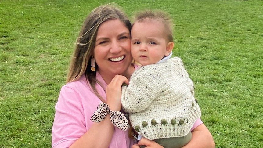 A woman in a pink shirt holds a baby with short spiky hair