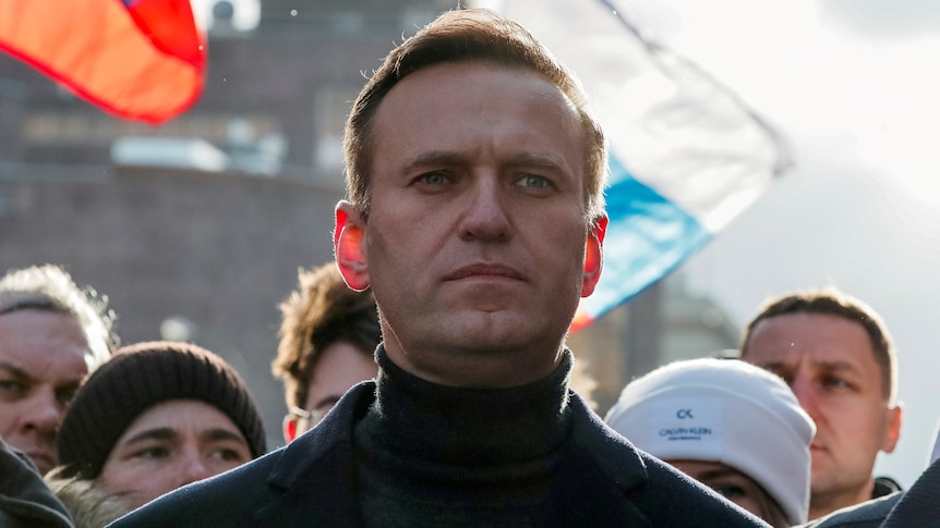 Alexei Navalny looks stoic, with supporters with flags behind him 