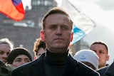 Alexei Navalny looks stoic, with supporters with flags behind him 