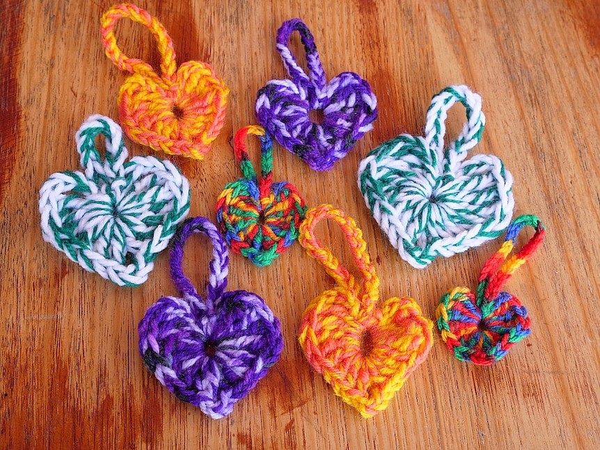 Eight colourful crocheted hearts laying flat on a table.