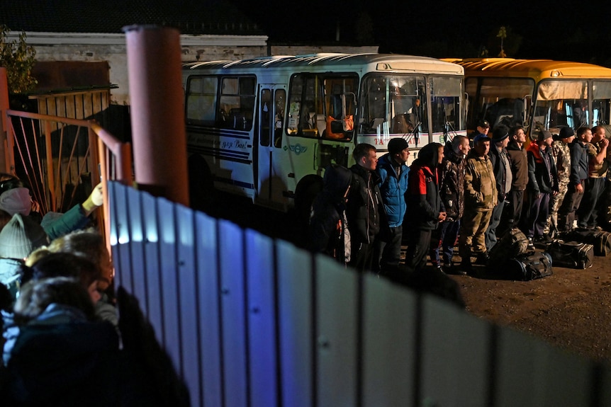 Recently mobilised reservists line up outside a recruitment office in front of busses.