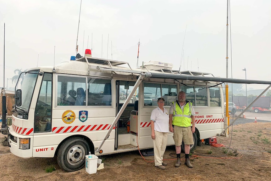 Two people stand outside a white bus