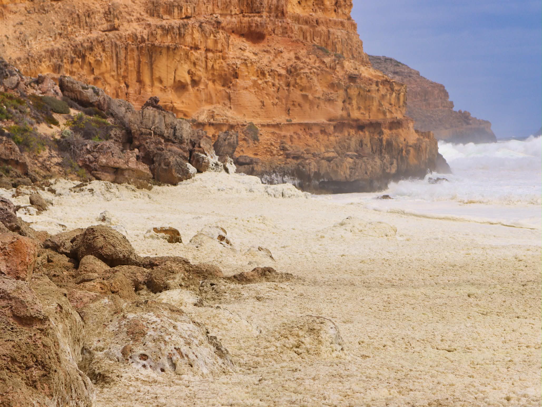 Agua marrón espumosa vista en una playa estrellándose contra rocas y un acantilado