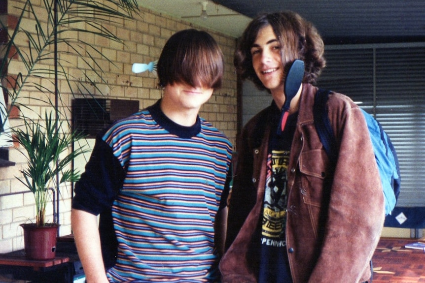 Two young boys stand together with long hair combed over their faces