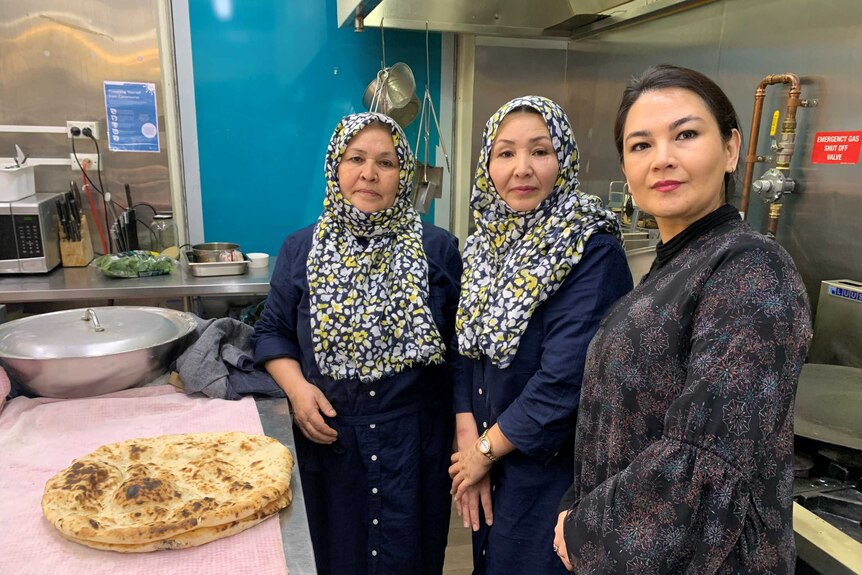 Three Afghan Hazara women, two hearing headscarfs in a commercial kitchen.