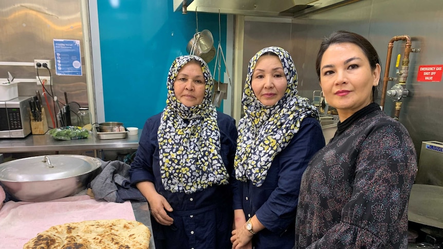 Three Afghan Hazara women, two hearing headscarfs in a commercial kitchen.