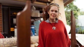 A woman with a red jumper smiles at the camera, front on.