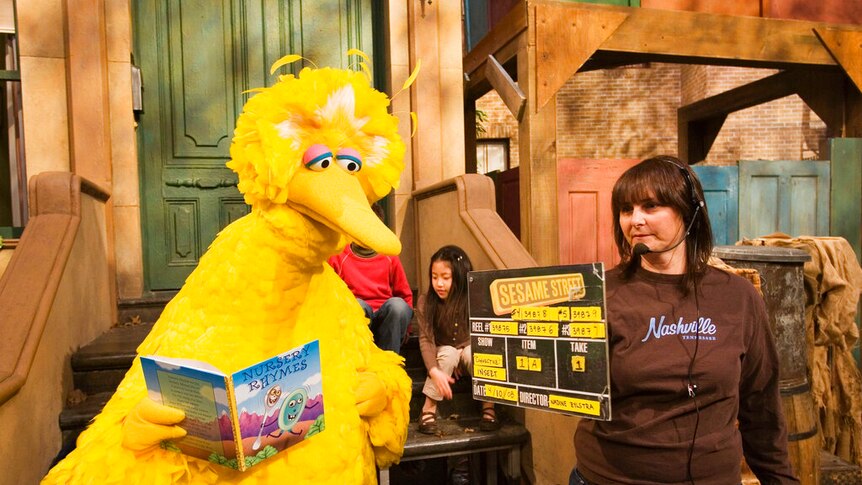 A wide photo shows the steps of the Sesame Street set with a bright yellow Big Bird sitting on the stoop.